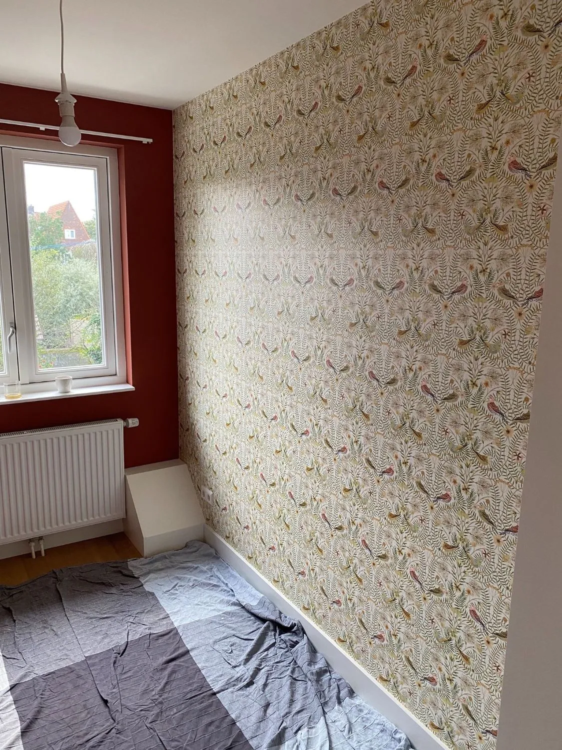 Wand met behang met vogels en bladeren naast een terracotta geschilderde wand met raam