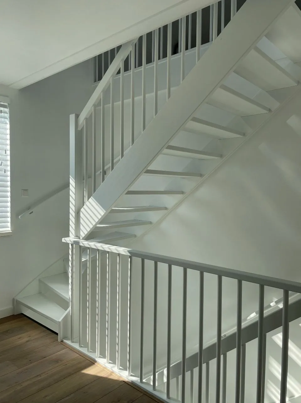 Wit gelakte open trap met spijlen en balustrade in een lichte hal